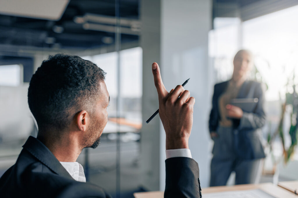 Young worker raise his finger up to ask a question to business team leader during seminar