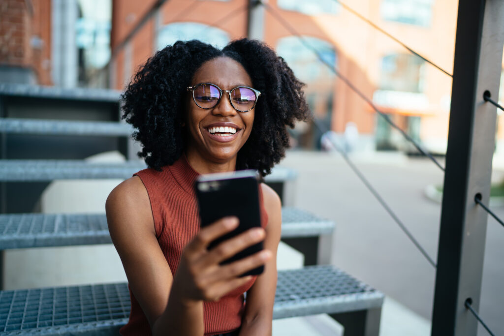 Cheerful black female using cellphone spending time in street