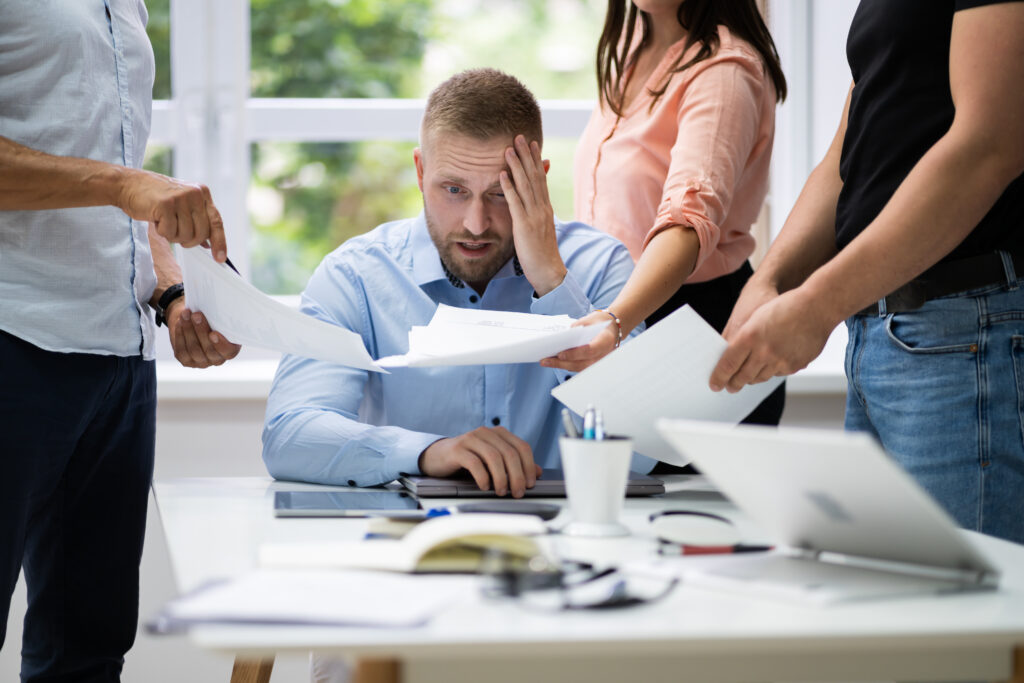 A stressed man in the office with people handing him papers